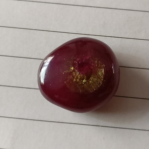 May include: A smooth, round, red stone with a gold and iridescent swirl in the center.