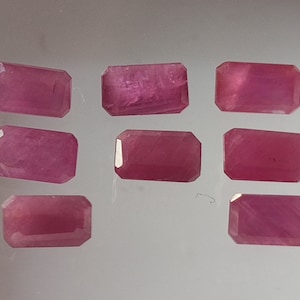 May include: Eight pink rectangular gemstones with a smooth, polished finish. The gemstones are arranged in three rows on a white surface.