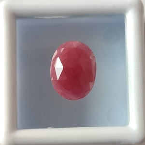 Può includere: Una pietra preziosa ovale rosa con taglio a faccette, esposta in una scatola bianca.
