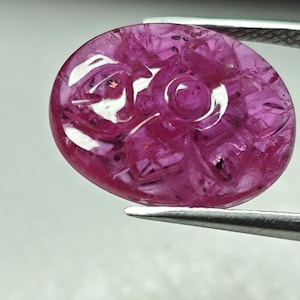 Peut inclure: Une pierre précieuse de rubis rose sculptée avec un motif floral. La pierre précieuse est de forme ovale et a un haut poli.