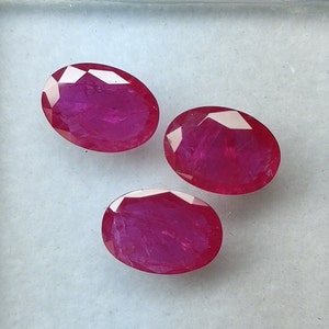 Puede incluir: Tres piedras preciosas de rubí de forma ovalada y facetadas. Los rubíes son de un color rojo intenso y rico.
