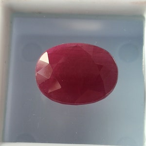 May include: A deep red oval gemstone with a faceted cut.