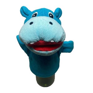 May include: A plush hand puppet shaped like a hippopotamus, featuring a bright blue body, a lighter blue snout, dark blue nostrils, black and white eyes, and a wide open mouth with a red interior and two small white teeth visible on the lower jaw.