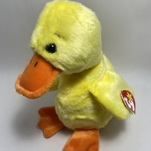May include: Yellow plush duck with an orange beak and feet. The duck has a small, black eye and a red star on the tag.
