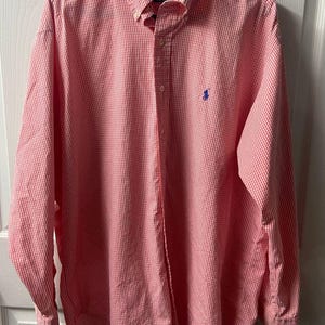 May include: A long-sleeve button-down shirt featuring a red and white gingham check pattern. The shirt includes a button-down collar, a front button placket, and a blue embroidered logo on the left chest. The interior label reads Ralph Lauren.