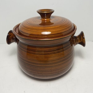 May include: A brown ceramic casserole dish with a lid. The dish has two handles and a lid with a knob. The exterior features horizontal brown and black stripes. The dish is designed for cooking and serving.