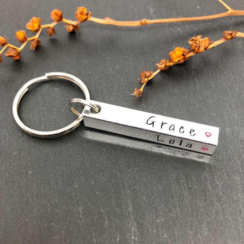 May include: Silver keychain with a bar charm engraved with the names "Grace" and "Lola" separated by a heart symbol.