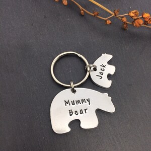 Puede incluir: Un llavero de plata con forma de oso con el texto "Mummy Bear" en un lado y un llavero m&aacute;s peque&ntilde;o con forma de oso con el texto "Jack" en el otro lado.