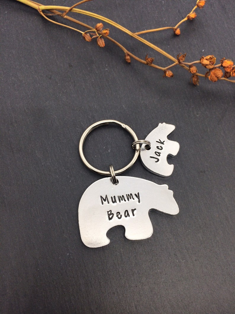 Puede incluir: Un llavero de plata con forma de oso con el texto "Mummy Bear" en un lado y un llavero m&aacute;s peque&ntilde;o con forma de oso con el texto "Jack" en el otro lado.