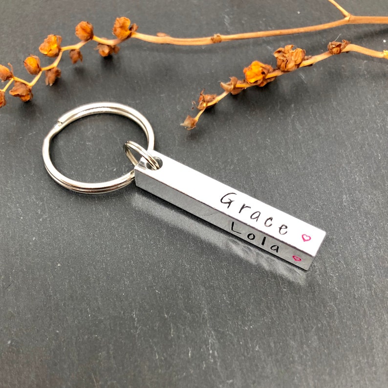 May include: Silver keychain with a bar charm engraved with the names "Grace" and "Lola" with a heart symbol after each name.