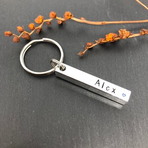 May include: Silver keychain with a bar charm engraved with the name "Alex" and a small blue heart.