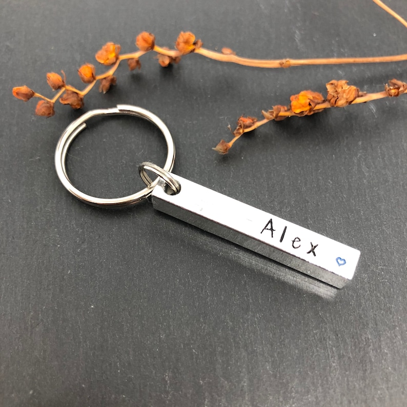 May include: Silver keychain with a bar charm engraved with the name "Alex" and a small blue heart.