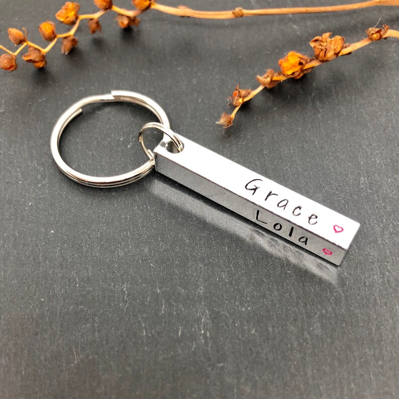 May include: Silver keychain with a bar charm engraved with the names "Grace" and "Lola" with a small pink heart symbol.