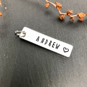 May include: Silver metal keychain with a rectangular tag that says "ANDREW" with a small heart symbol.