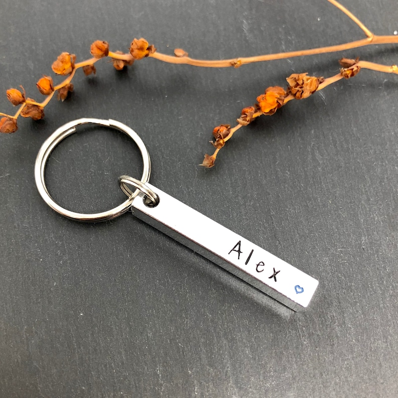 May include: Silver keychain with a bar charm engraved with the name "Alex" and a small blue heart.