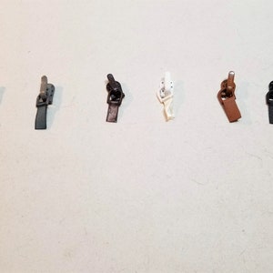 Könnte beinhalten: Sortiment von sieben Reißverschluss-Zierbändern in verschiedenen Farben, darunter Schwarz, Braun, Beige und Weiß.