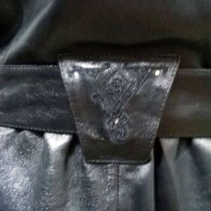 Pu&ograve; includere: Una giacca di pelle nera con una cintura decorativa con un design intricato. La cintura ha una fibbia con un piccolo ornamento argentato.