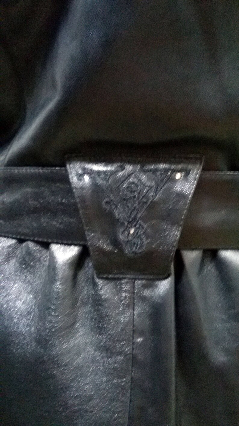 Pu&ograve; includere: Una giacca di pelle nera con una cintura decorativa con un design intricato. La cintura ha una fibbia con un piccolo ornamento argentato.