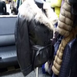 Pu&ograve; includere: Una giacca di pelle nera con colletto di pelliccia e cintura. La giacca &egrave; su un manichino in un negozio.