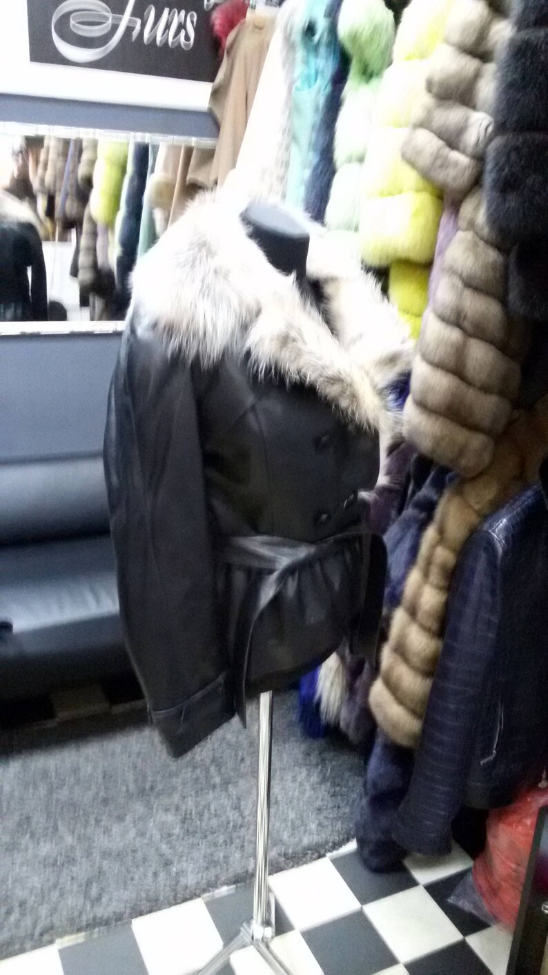 Pu&ograve; includere: Una giacca di pelle nera con colletto di pelliccia e cintura. La giacca &egrave; su un manichino in un negozio.