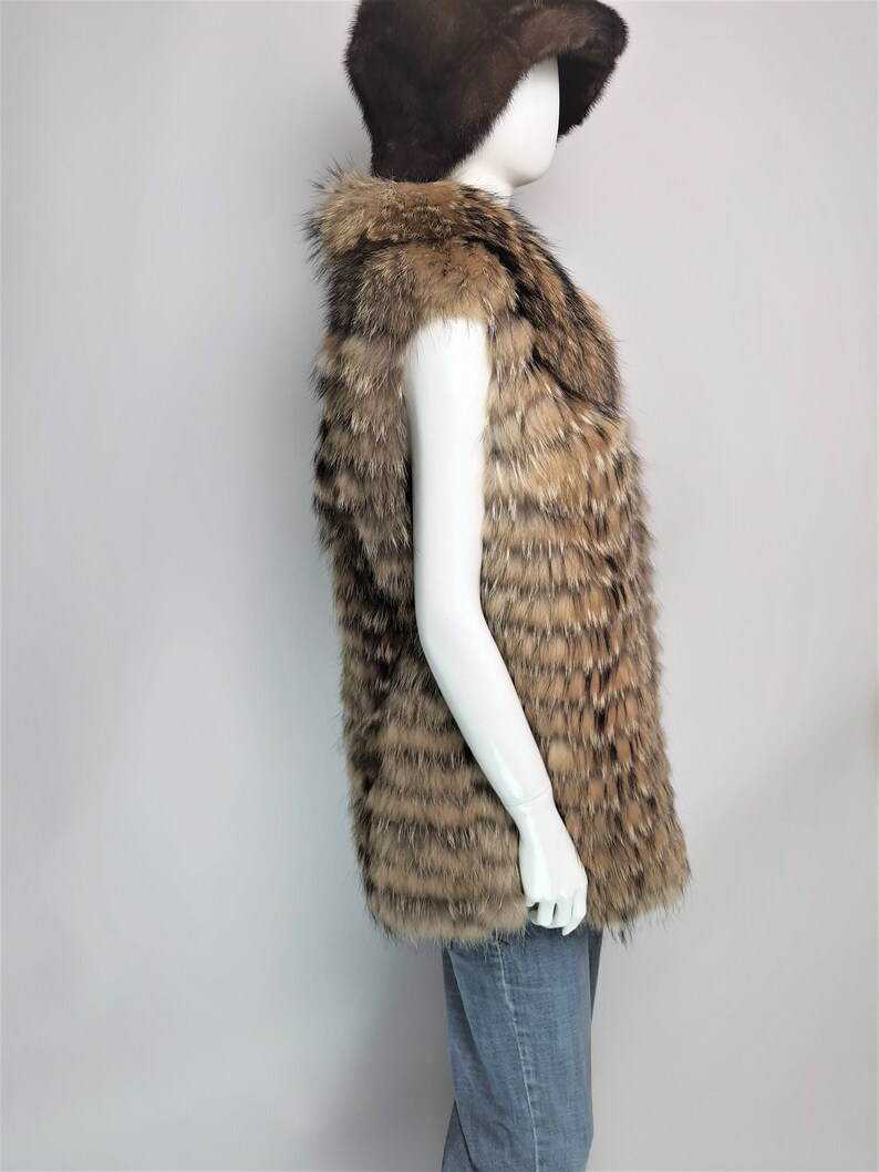 May include: A brown and tan fur vest with a sleeveless design. The vest is made of a soft, fluffy fur and has a long, flowing style.