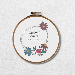 Puede incluir: Aro bordado con fondo blanco y una corona floral negra. La corona rodea el texto "Dios dirigirá tus pasos - Proverbios 16:9".