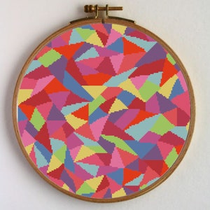 Puede incluir: Un patrón geométrico colorido de triángulos en tonos de rojo, rosa, azul, amarillo y verde, cosido en un aro de bordado circular.