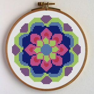 Puede incluir: Un aro de bordado de punto de cruz con un diseño de mandala colorido. El mandala presenta un centro azul con un diseño de flor rosa y anillos exteriores verdes y morados.