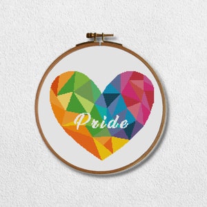 Peut inclure: Un cercle de broderie au point de croix avec un cœur géométrique aux couleurs de l'arc-en-ciel. Le mot "Pride" est brodé en blanc sur le cœur. Le cercle en bois est monté sur un fond blanc.