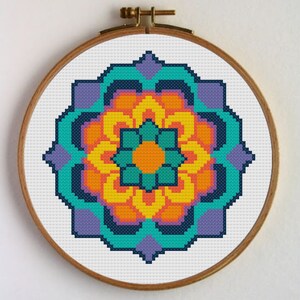 Puede incluir: Un patrón de punto de cruz mandala colorido con un esquema de color turquesa, naranja, amarillo y morado. El diseño presenta una forma de flor con detalles intrincados.