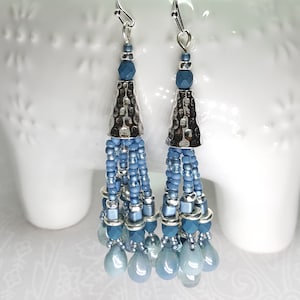 May include: Silver tone dangle earrings with blue glass beads and a hammered metal cone. The earrings have a tassel-like design.