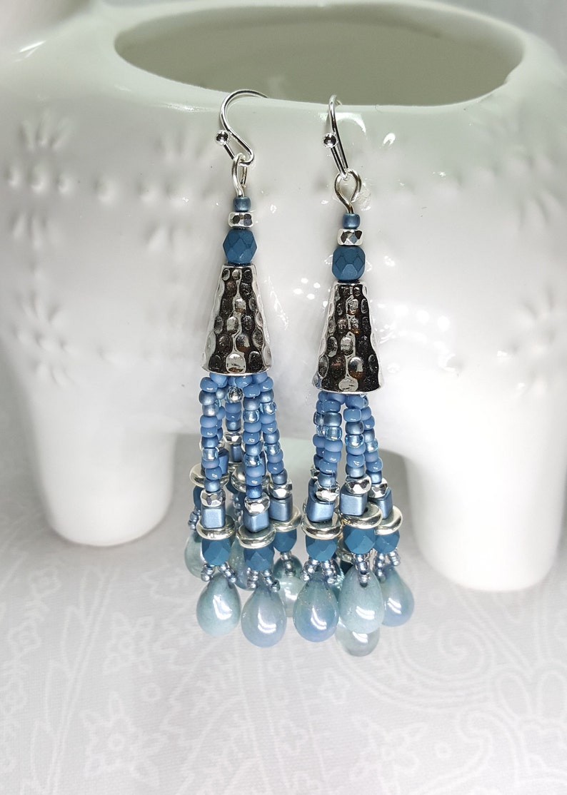 May include: Silver tone dangle earrings with blue glass beads and a hammered metal cone. The earrings have a tassel-like design.