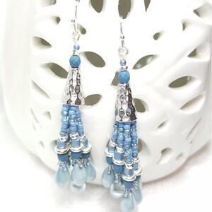 May include: A pair of silver dangle earrings with blue glass beads and a silver cone charm. The earrings are hanging from a white background.