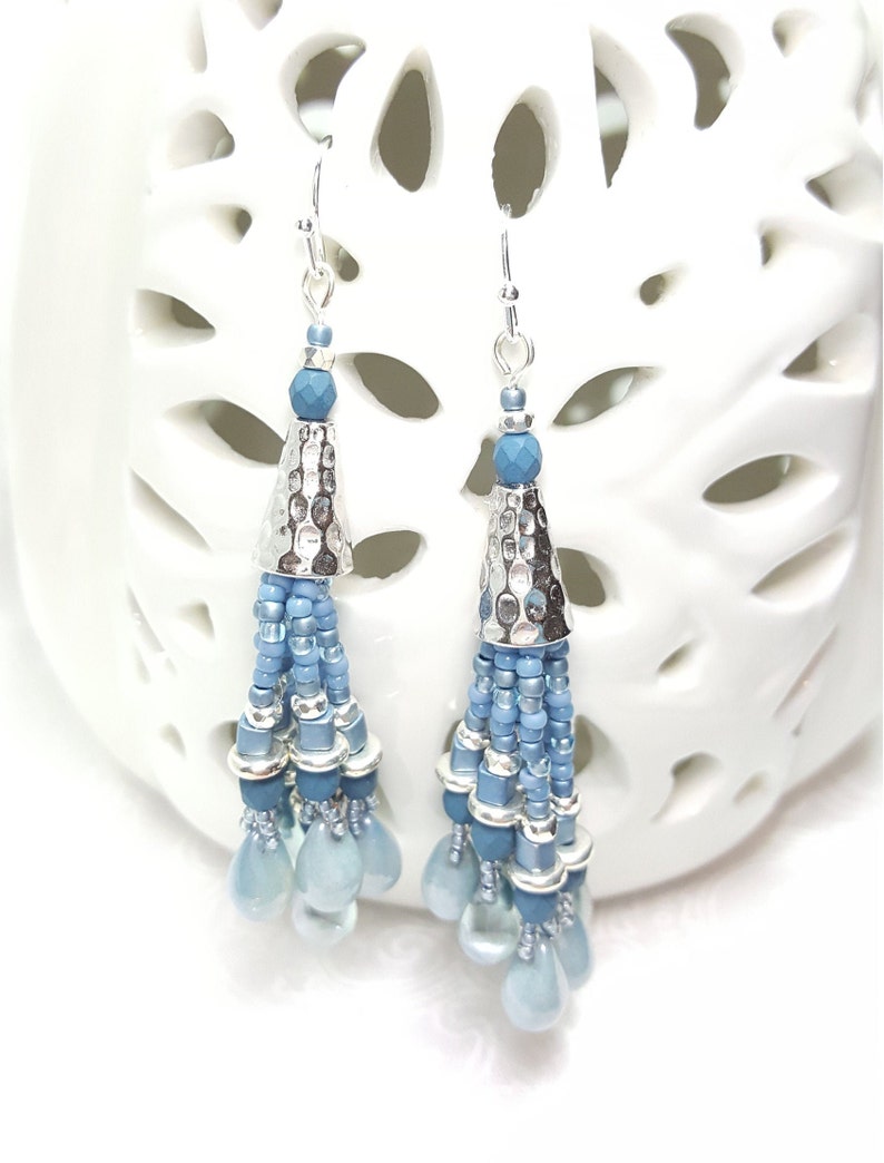 May include: A pair of silver dangle earrings with blue glass beads and a silver cone charm. The earrings are hanging from a white background.
