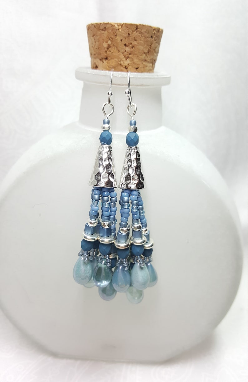 May include: Silver and blue beaded tassel earrings with a hammered metal cone at the top.