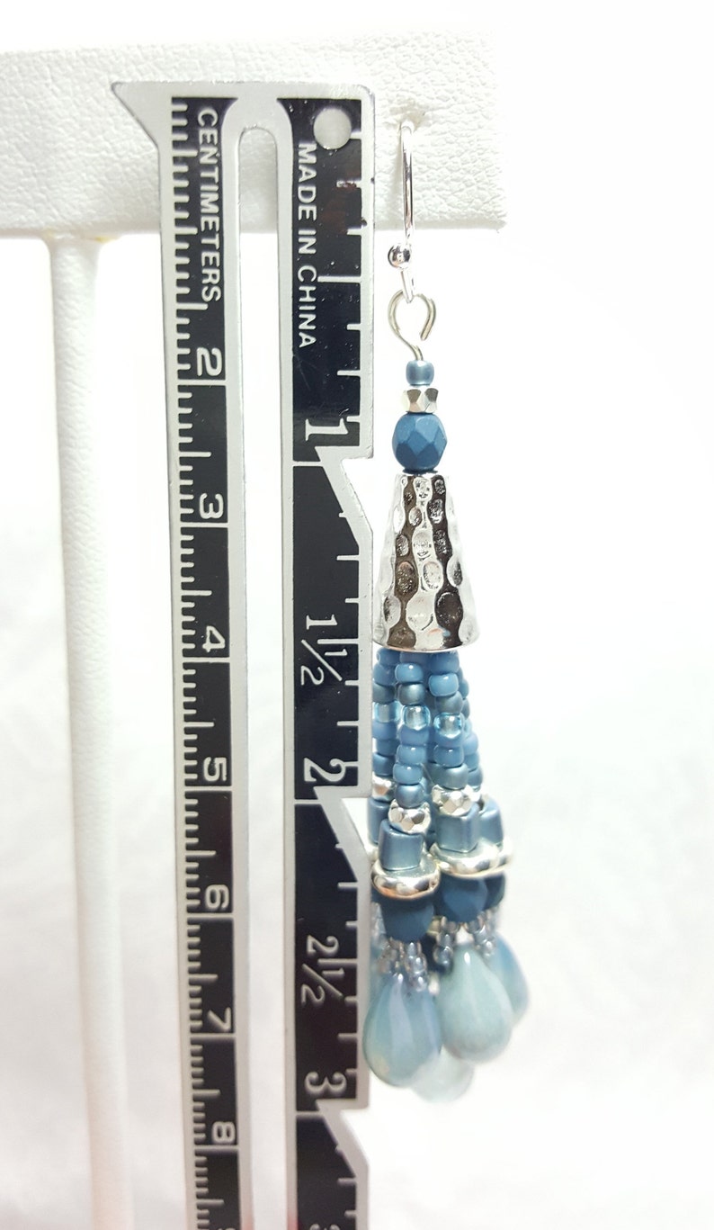 May include: Blue and silver beaded dangle earrings with a hammered metal cone charm. The earrings measure approximately 3 inches in length.