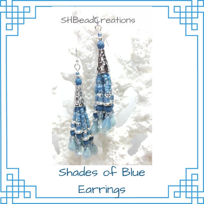 May include: Shades of Blue Earrings, a pair of long, beaded earrings with silver accents and blue beads in various shades. The earrings are hanging from a white background.