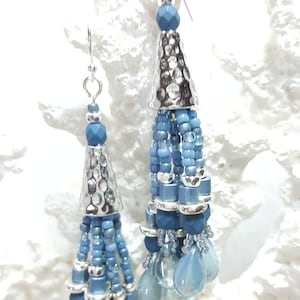 May include: A pair of silver and blue beaded tassel earrings. The earrings feature a silver cone-shaped charm with a hammered texture and a tassel of blue beads.
