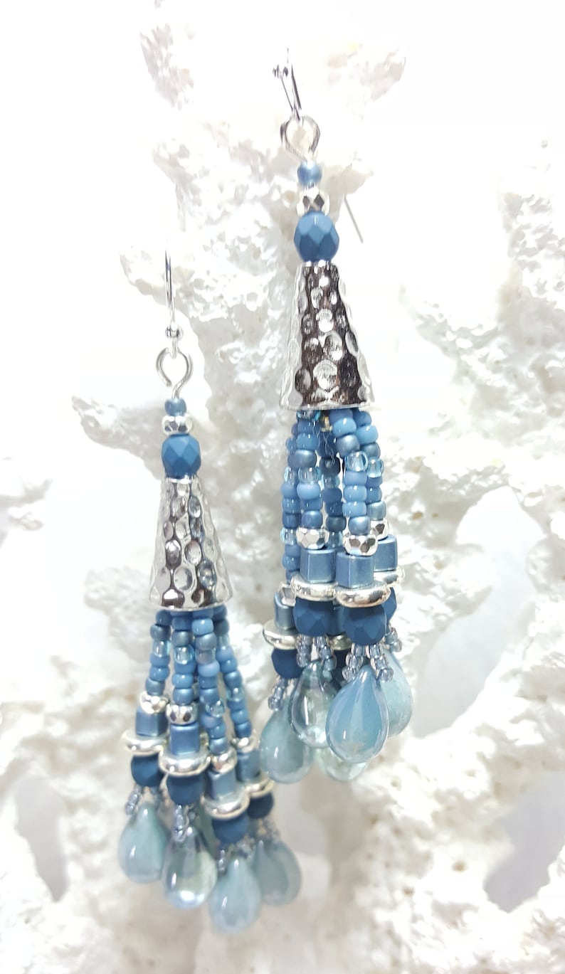 May include: A pair of silver and blue beaded tassel earrings. The earrings feature a silver cone-shaped charm with a hammered texture and a tassel of blue beads.