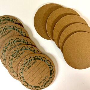 May include: Ten brown paper circles with green borders and the text "Artist Trading Coin" printed on them. The text "Handmade Art" is printed on one of the circles.