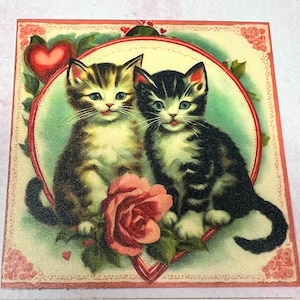 May include: Vintage Valentine's Day card featuring two kittens with a red heart and a pink rose. The kittens are sitting next to each other and looking at the viewer. The card has a white background with a pink border.