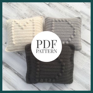 May include: Three crocheted pillow covers in beige, gray, and dark gray with a textured stitch pattern and a raised center square. The image includes the text "PDF PATTERN".