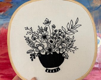 May include: Black and white embroidery of a floral arrangement in a vase, framed in a wooden hoop.