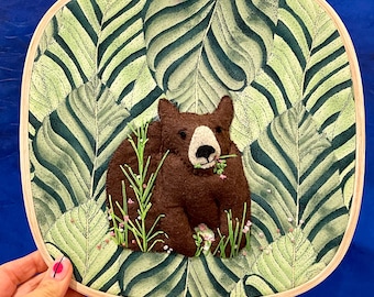 A big brown bear in the forest eating flowers - 10 inch square hoop