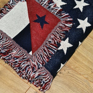 May include: A folded throw blanket with a patriotic design. The blanket features a red, white, and blue color scheme with a star pattern and fringe trim. The blanket is made of a woven material.