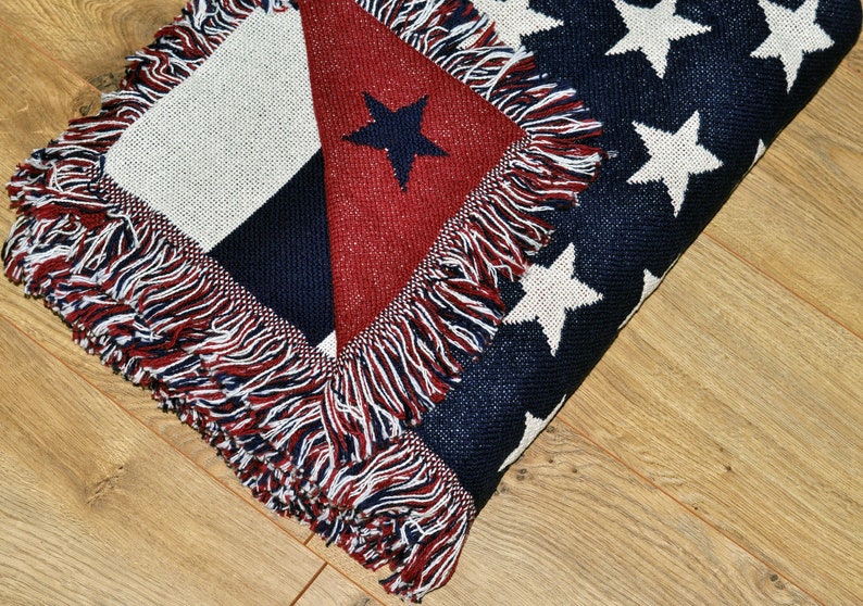 May include: A folded throw blanket with a patriotic design. The blanket features a red, white, and blue color scheme with a star pattern and fringe trim. The blanket is made of a woven material.