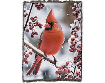 May include: A red cardinal perched on a snow-covered branch with red berries. The bird is facing left and has a black eye and beak. The background is a snowy winter scene.