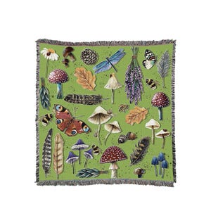 May include: A green throw blanket featuring a whimsical design of forest elements. The design includes mushrooms, butterflies, leaves, feathers, and insects. The blanket has a fringed edge and is suitable for a bed or sofa.