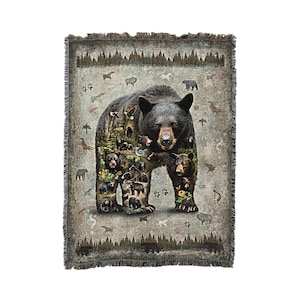 May include: A woven tapestry throw blanket featuring a black bear with a woodland scene inside its silhouette. The bear is standing on a forest floor with trees and other animals in the background.