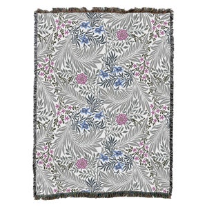 May include: A woven throw blanket with a floral pattern in shades of grey, pink, and blue. The pattern features stylised leaves and flowers.